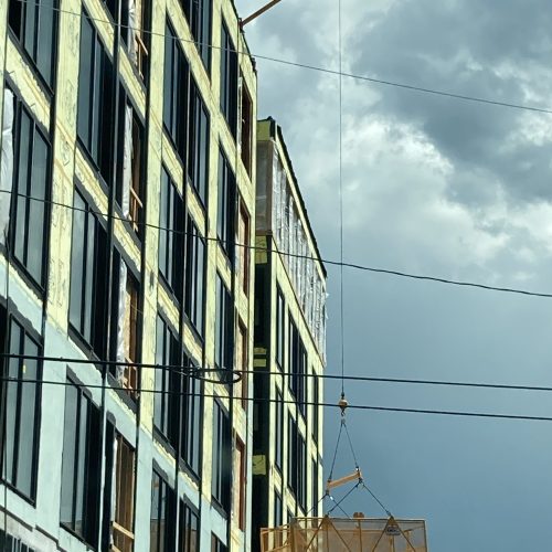 A DOC® Material Basket is being used to access inner floors of a 5-story construction project through window openings. A DOC® Material Hoist is installed on the roof using cribbing and other methods.
