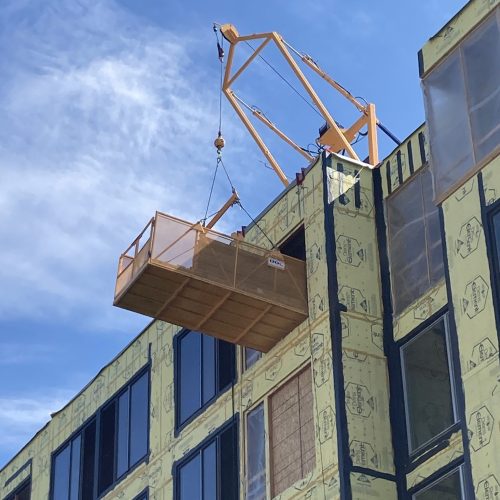 A DOC® Material Basket used to access inner floors of a 5-story construction building. A DOC® Material Hoist is installed on the roof of the building providing hook access to inner floors.